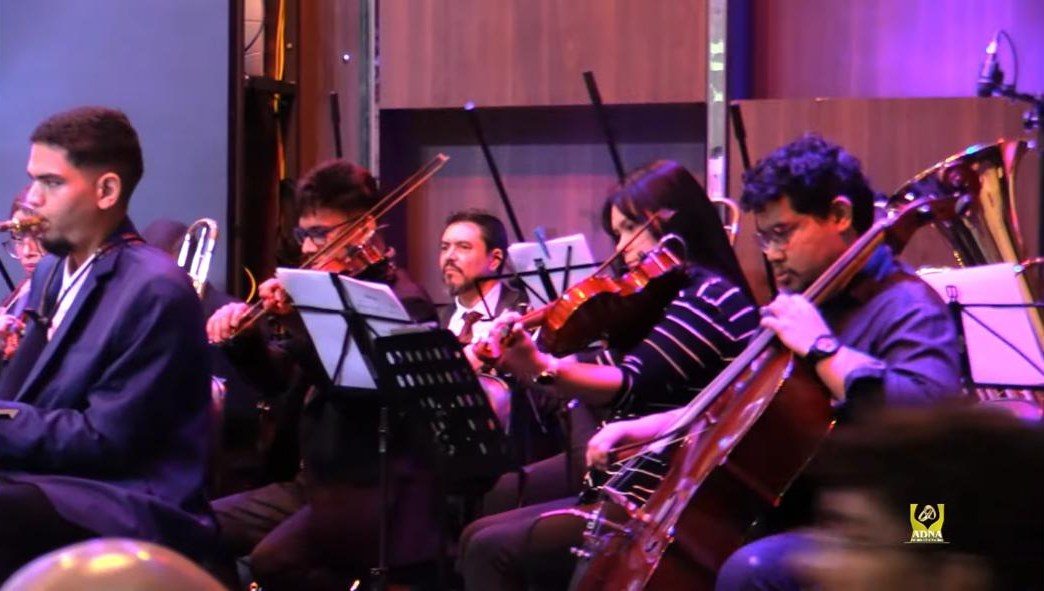 Naipe de cordas em apresentação com orquestra, com Roney ao violoncelo